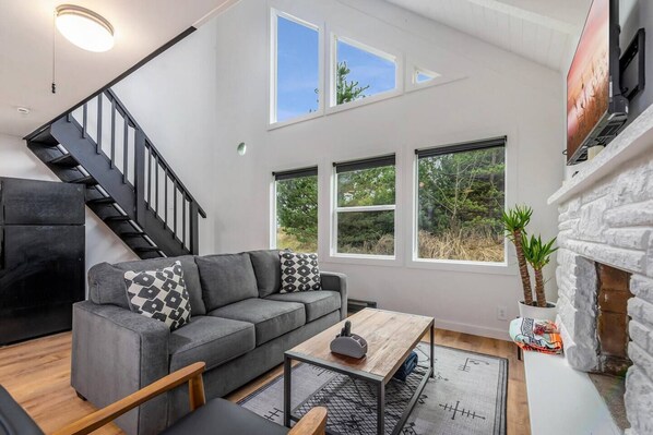 Ein modernes Wohnzimmer mit einem grauen Ecksofa, einem Holztisch und einer Treppe mit schwarzen Geländern.