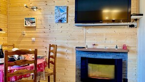 A cozy room with a wooden interior, a flat-screen TV mounted on the wall, a fireplace, and a dining area with a table and chairs. - 4-person apartment - all comforts <br>Skis at your feet (La Joue du loup - Le Devoluy)