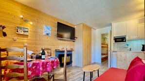 A cozy room with a wooden floor, a dining table with chairs, a red sofa, a TV mounted on the wall, and a kitchen area with a microwave. - 4-person apartment - all comforts <br>Skis at your feet (La Joue du loup - Le Devoluy)