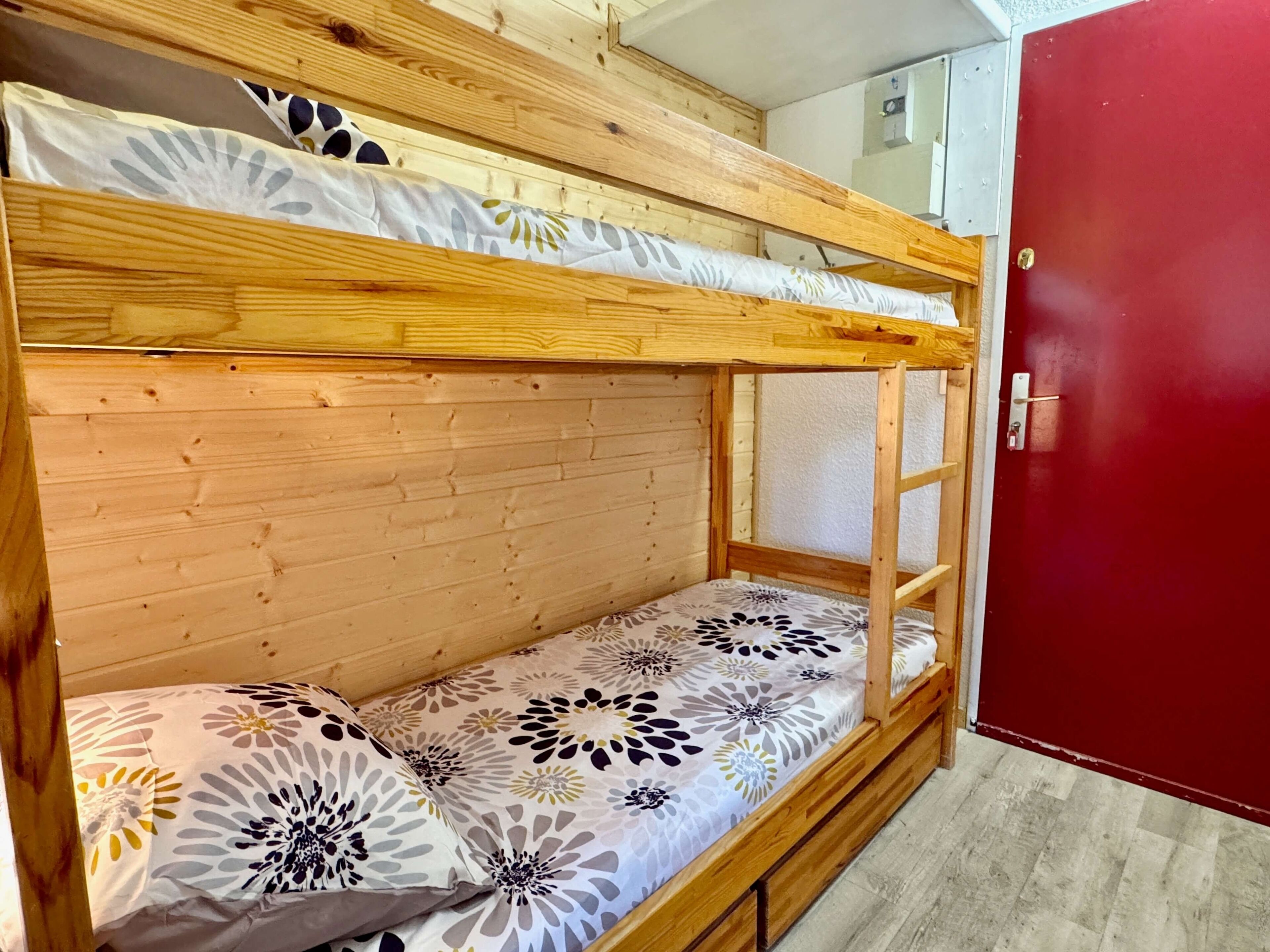A bunk bed with floral bedding, wooden headboard, and a red door.