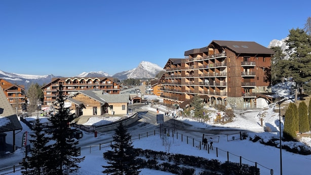 A snow-covered resort with wooden buildings, ski slopes, and a mountain backdrop. - 4-person apartment - all comforts <br>Skis at your feet (La Joue du loup - Le Devoluy)