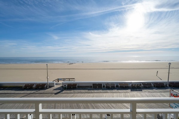 Une vue sur la plage depuis un balcon doté d’une terrasse en bois, de bancs et d’une enseigne indiquant l’emplacement d’une boutique de beignets.