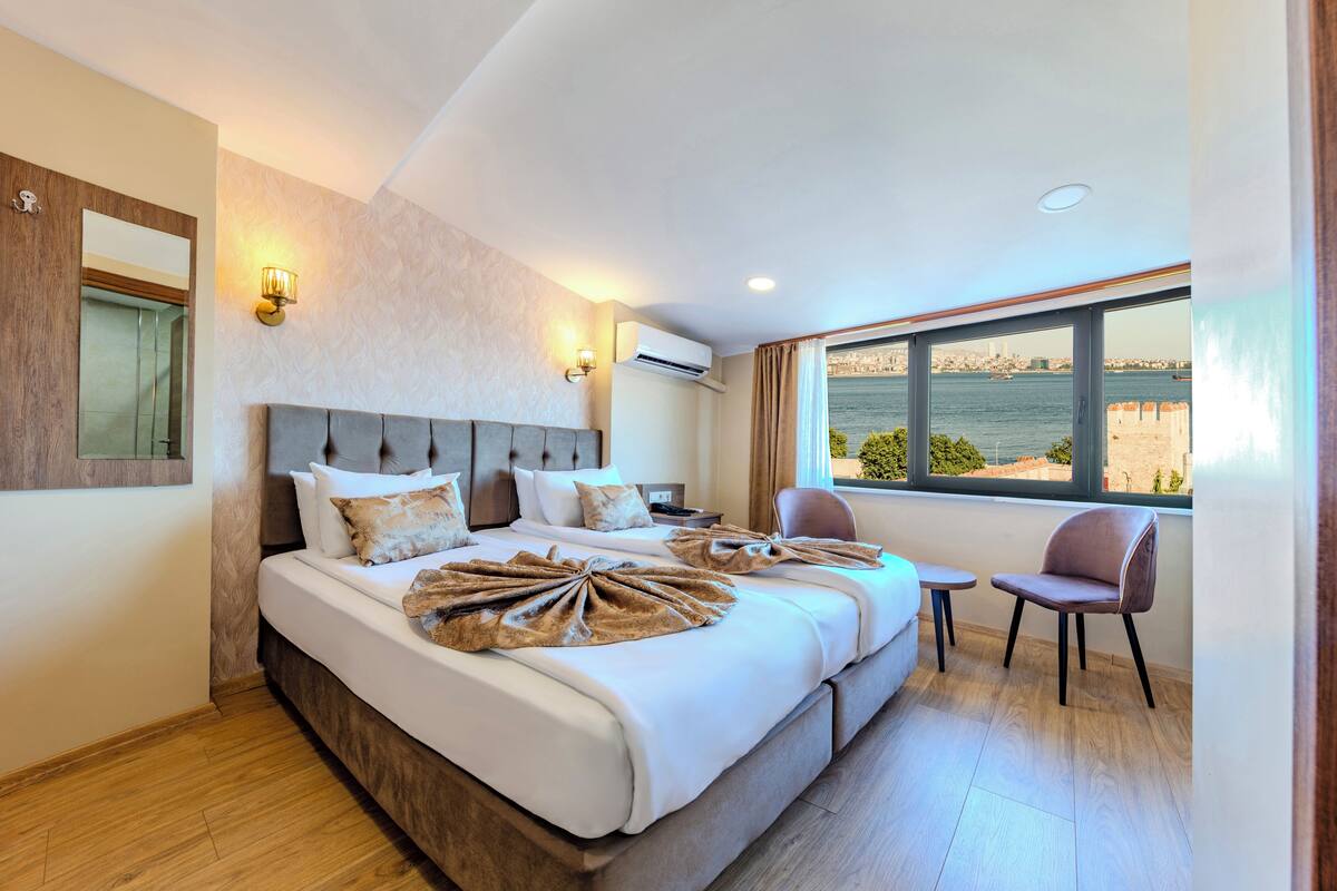 A hotel room with a large bed, a view of the sea, a small table, and a chair.
