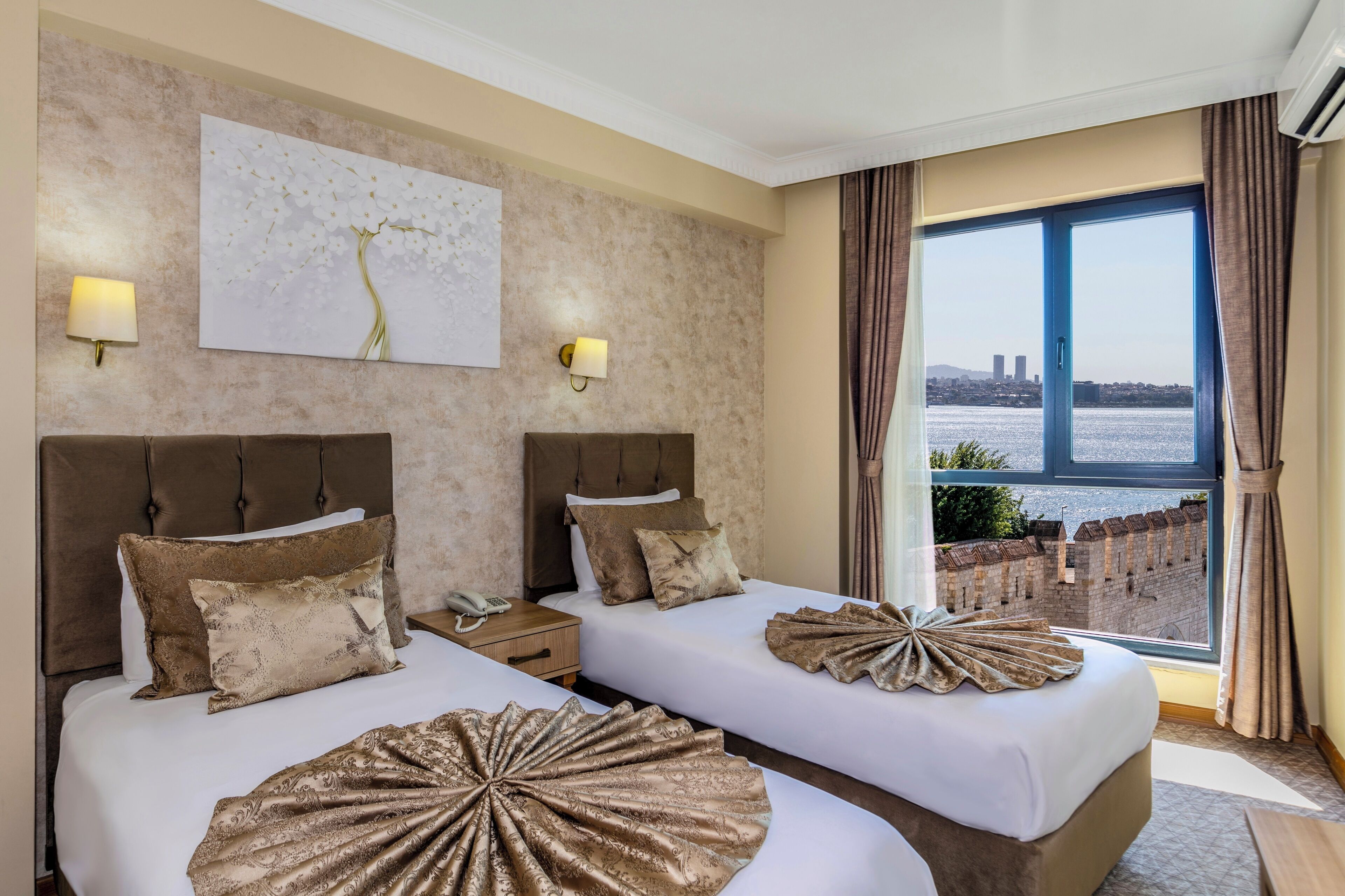 A hotel room with two beds, a large window with a view of a city and a river, and a decorative wall piece.