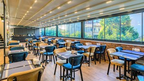 A modern restaurant with multiple tables and chairs, large windows with a view of greenery, and a brick wall. - Sultan Hamit Hotel (Istanbul)