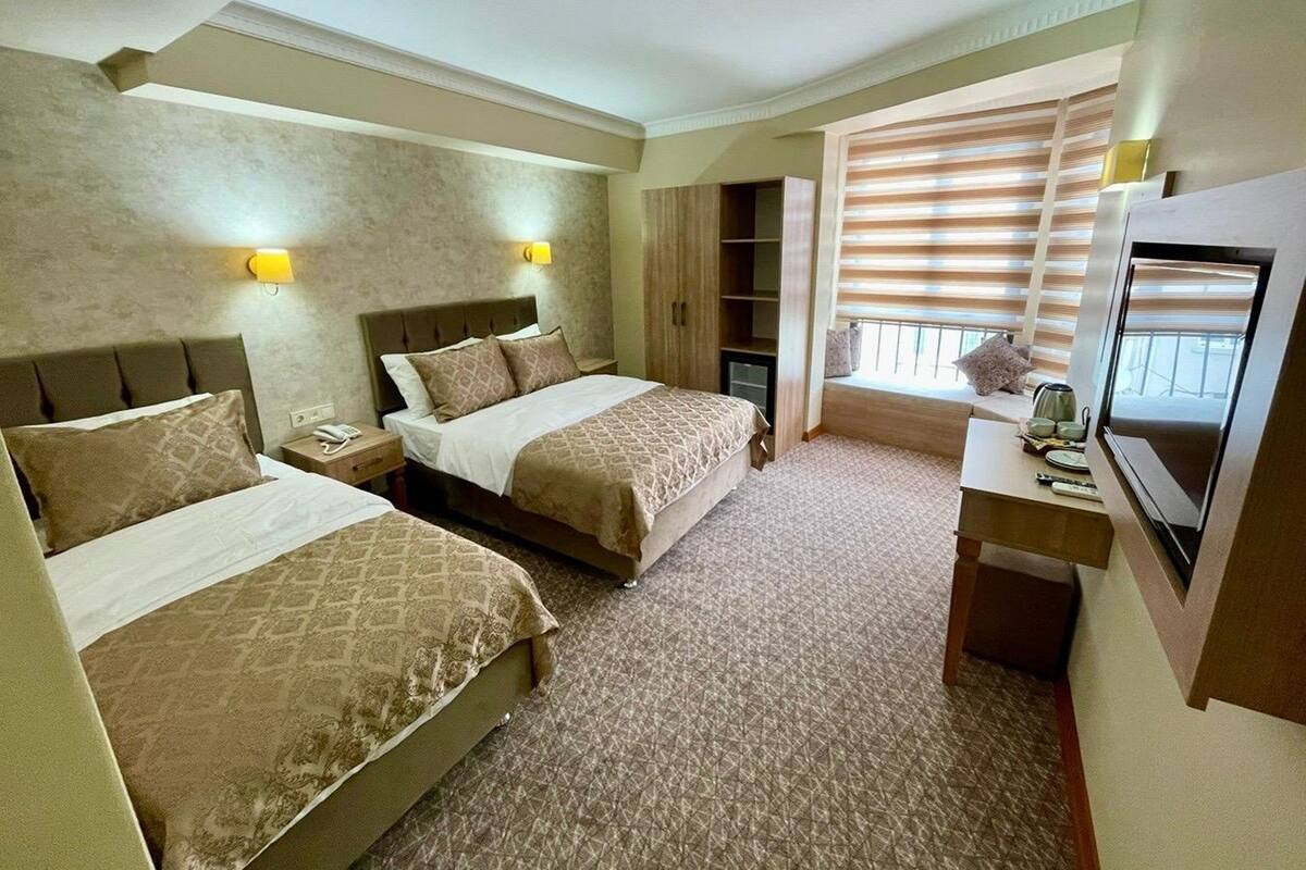 A hotel room with two beds, a desk with a TV, and a window with blinds.