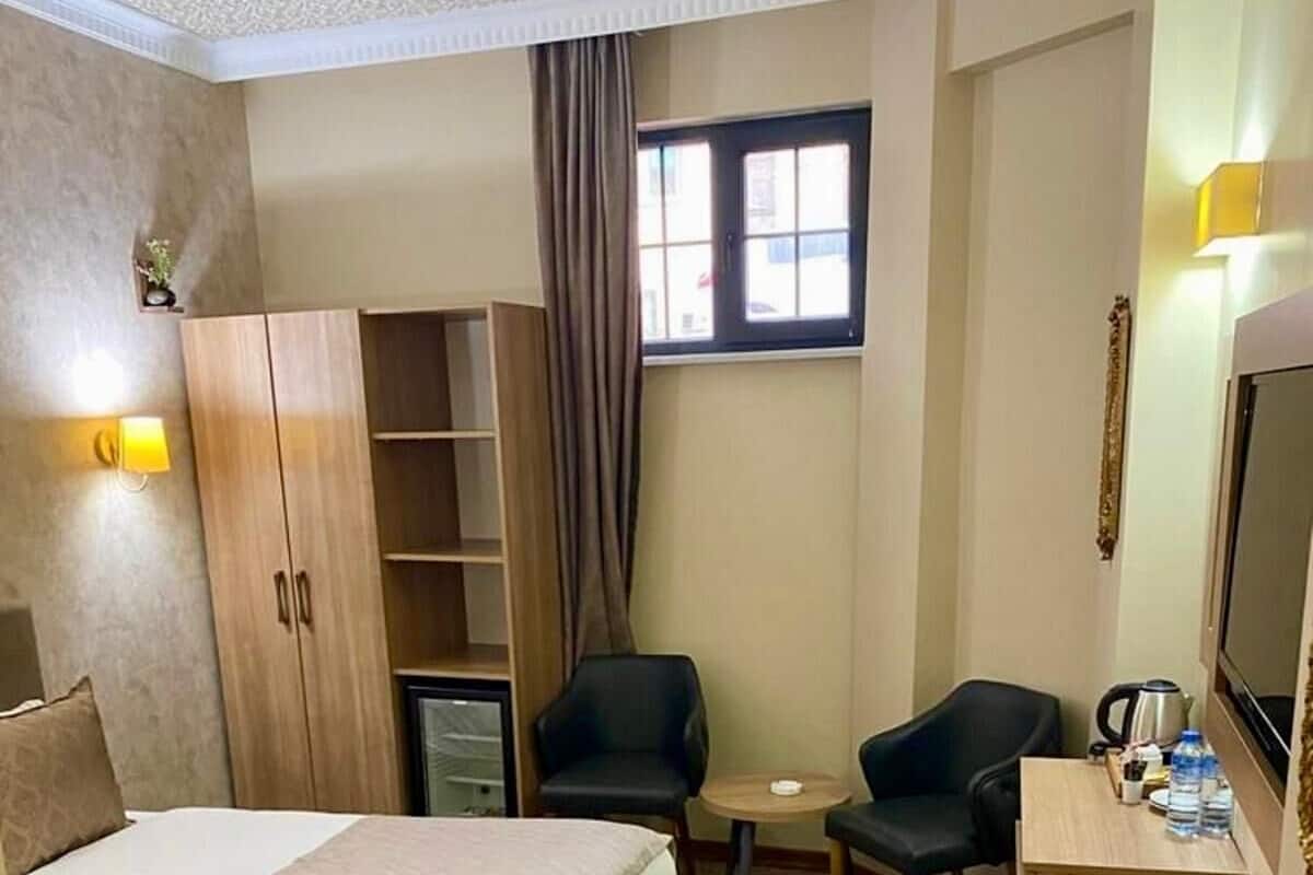 A hotel room with two beds, a desk, a chair, a small table, a television, and a wardrobe.