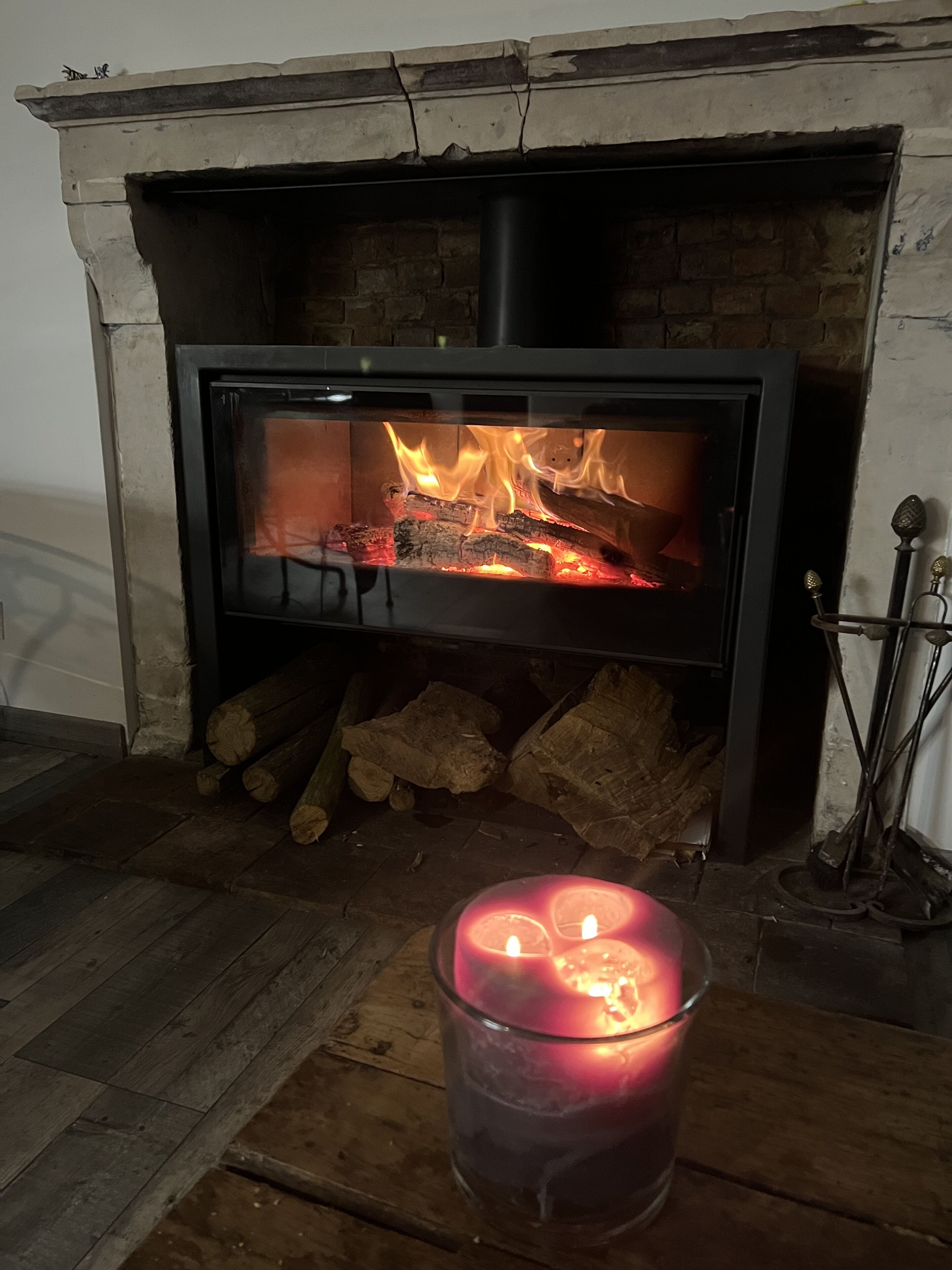Una chimenea con puerta de cristal, leña y un candelabro.