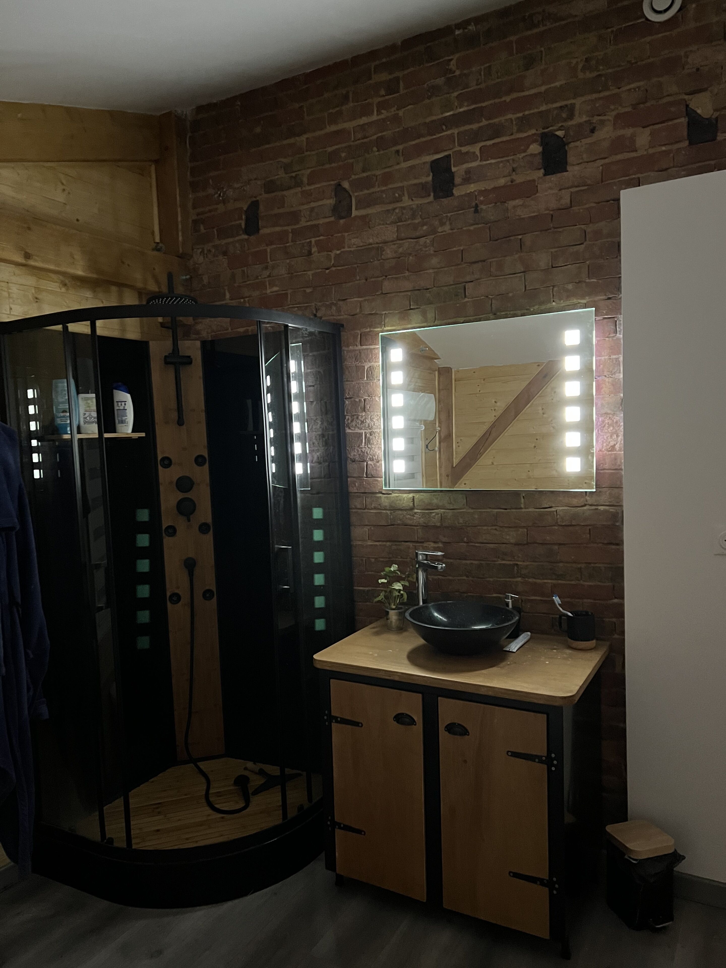 Ein kleines Badezimmer mit einem Holzkosmetikschrank, einem schwarzen Waschbecken und einem beleuchteten Spiegel.