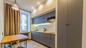 A compact kitchen with a wooden table and chairs, grey cabinets, and a window with curtains. - Idea Design Apart-Hotel Prorizna (Kyiv)