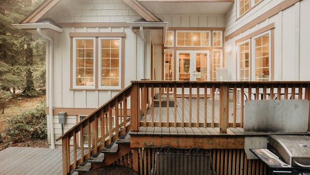 A two-story house with a wooden deck, a staircase, and a grill.
