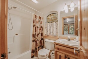A bathroom with a shower, toilet, sink, and a window with a view of trees. - Snowline Cabin #34 - Great English Tudor-style Home With hot Tub! Now With Wifi! (Deming)