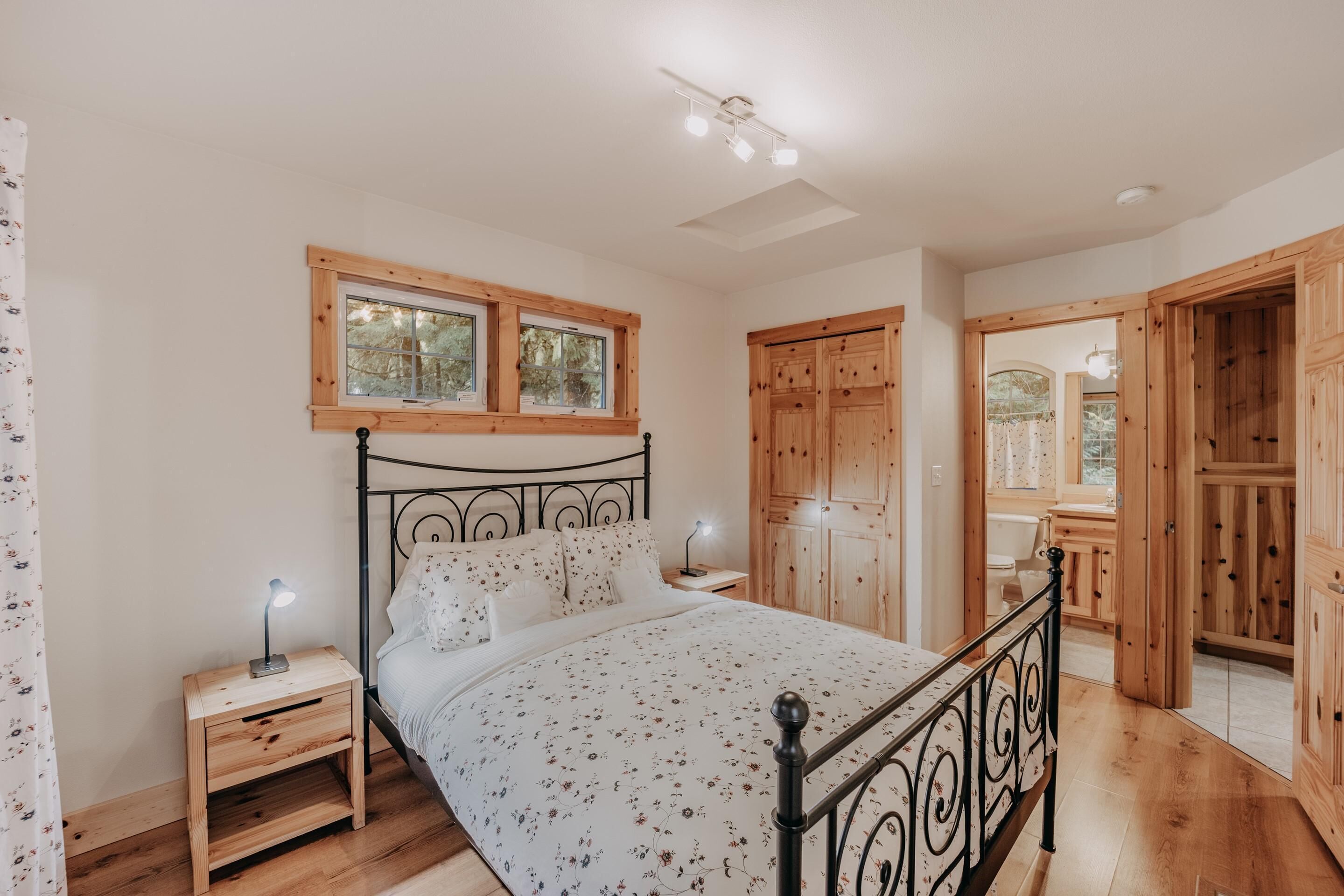 A bedroom with a bed, wooden nightstands, a desk, a window, and a wardrobe.