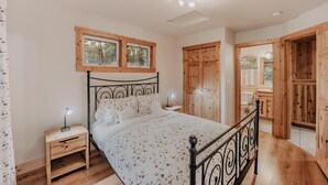 A bedroom with a bed, wooden nightstands, a desk, a window, and a wardrobe.