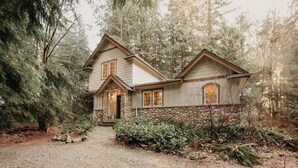 A two-story house with a stone foundation and a wooden upper structure, surrounded by dense forest.