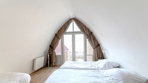 A room with two beds, a radiator, and a window with curtains. - Flat Fish (Egmond aan Zee)