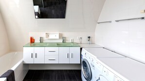 A modern bathroom with a glass sink, white cabinets, a black bathtub, and a front-loading washing machine. - Flat Fish (Egmond aan Zee)