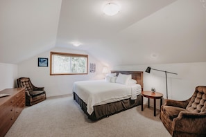 Une chambre à coucher avec un grand lit, un bureau, deux chaises, une lampe et une fenêtre.