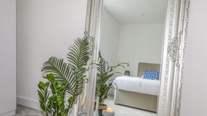 A bedroom with a large ornate mirror, a bed with a blue and white pillow, and two potted plants. - Bryn Min Manton Apartment (Caernarfon)