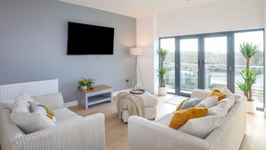 A modern living room with a large flat-screen TV, two sofas, a coffee table, and a floor lamp. - Bryn Min Manton Apartment (Caernarfon)