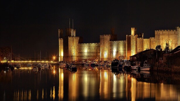 A historic castle with a moat, illuminated by artificial lighting, reflecting in the water. - Bryn Min Manton Apartment (Caernarfon)