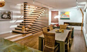 Cozy dining area with a wooden table and wicker chairs, a sofa set, and a fireplace.