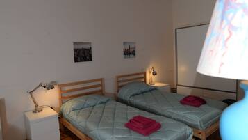 A room with two beds, a nightstand with a lamp, and a wall-mounted TV.