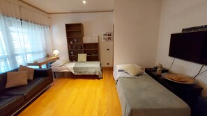 A room with two beds, a sofa, a TV, a bookshelf, and a desk.