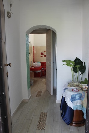 A hallway with a tiled floor, a door on the left, and a table with a plant on the right. - Room in Guest Room - S'olivariu Village Affittacamere - Junior Suite Terrace (Piscinas)