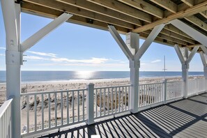 A beach view from a covered deck with white railings and a wooden floor.