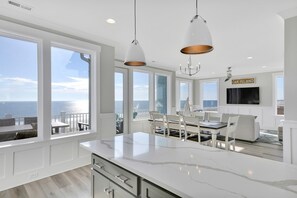 A modern kitchen with large windows, a dining area, and a view of the ocean.