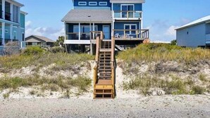 Ett hus i flera våningar som ligger vid stranden, med en trätrappa som leder upp till en balkong.