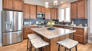 A modern kitchen with wooden cabinets, stainless steel appliances, a granite island with bar stools, and pendant lighting. - Experience luxury at 'Gratitude' in Oak Island, a spacious 5-bedroom ocean-view retreat. (Oak Island)