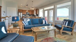 A spacious living area with a sofa set, a coffee table, and a view of the kitchen and outside. - Experience luxury at 'Gratitude' in Oak Island, a spacious 5-bedroom ocean-view retreat. (Oak Island)