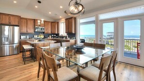 A modern kitchen with wooden cabinets, stainless steel appliances, a glass dining table, and a view of the ocean through large windows. - Experience luxury at 'Gratitude' in Oak Island, a spacious 5-bedroom ocean-view retreat. (Oak Island)