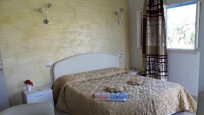 A bedroom with a bed, bedside tables, a nightstand, a chair, and a window with curtains. - Room in Guest Room - S'olivariu Village Affittacamere - Deluxe King Room (Piscinas)