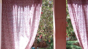 A room with a table and a chair, a window with floral curtains, and a view of greenery outside. - Room-sa Domu Sarda - Apartment With Terr (Piscinas)