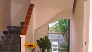 A hallway with a staircase, a table with a vase of sunflowers, and large green plants. - Room-sa Domu Sarda - Apartment With Terr (Piscinas)