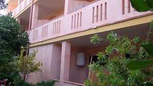 A multi-story building with balconies, a water tank, and surrounding greenery. - Room-sa Domu Sarda - Apartment With Terr (Piscinas)