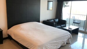 A modern hotel room with a large bed, a dark headboard, a small sofa, a table, and a balcony with chairs. - Platinum Suites Floor 6 Room 63 (Pattaya)