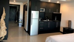 A modern kitchen with dark cabinets, a refrigerator, and a microwave. - Platinum Suites Floor 6 Room 63 (Pattaya)
