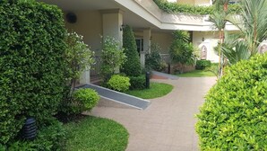 A pathway flanked by well-maintained greenery and a building with a covered entrance. - Nordic Park Hill Residence Flat (Pattaya)