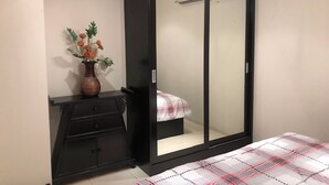 A bedroom with a black wardrobe, a bedside table with a vase of flowers, and a bed with a plaid bedspread. - Nordic Park Hill Residence Flat (Pattaya)