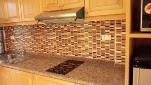 Una cocina con armarios de madera, una campana extractora de acero inoxidable, un salpicadero de azulejos y encimera de granito.