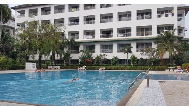 Una piscina con sillas de descanso y un edificio con balcones al fondo.