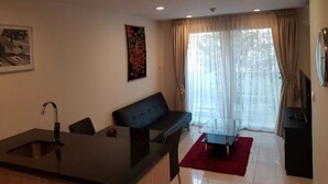A modern living room with a sofa, a glass coffee table, a red rug, a painting on the wall, and a TV on a stand.