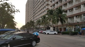 A multi-story building with balconies, palm trees, and parked cars on the street. - Jomtien Beach Condominium A2 Floor 12 Room 19 Studio (Pattaya)
