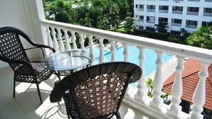 A balcony with a glass table and two wicker chairs, overlooking a swimming pool and a building with multiple balconies. - Baan Suan Lalana Sa Floor 5 Room 516 (Pattaya)