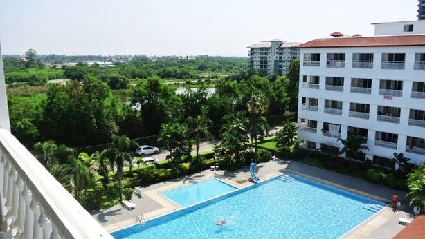 A swimming pool with a slide, surrounded by greenery and adjacent to a white building with balconies. - Baan Suan Lalana Sa Floor 5 Room 516 (Pattaya)