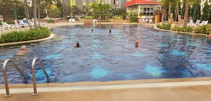 A swimming pool with multiple people in the water, surrounded by lounge chairs and palm trees.